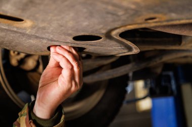 bare caucasian hand unscrews the drain plug of the engine crankcase to change the oil