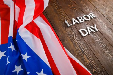 Tahta yüzeyde gümüş metal harflerle, sol tarafında buruşuk Amerikan bayrağıyla...