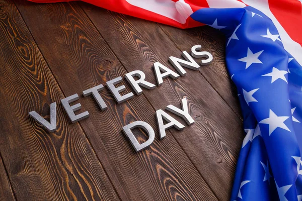 The words veterans day laid with silver metal letters on wooden board surface with crumpled usa flag at right side with diagonal perspective — Stock fotografie