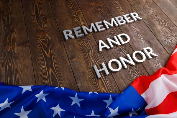 Words remember and honor laid with silver metal letters on wooden background with USA flag underneath Stockfoto