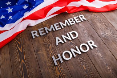 words remember and honor laid with silver metal letters on wooden background with USA flag above