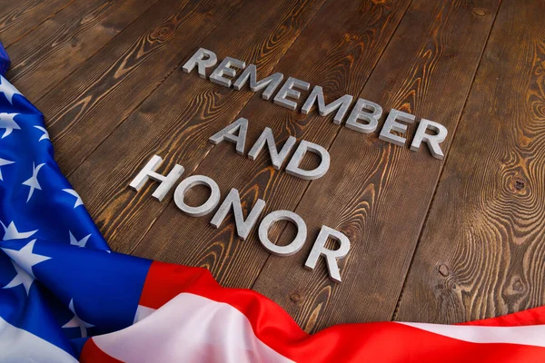 Words remember and honor laid with silver metal letters on wooden background with USA flag underneath — Stockfoto