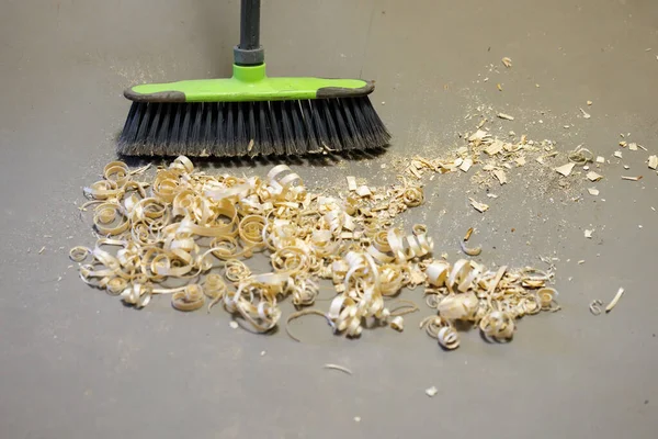 A small pile of wood shavings on a gray linoleum floor with a broom brush — Fotografia de Stock