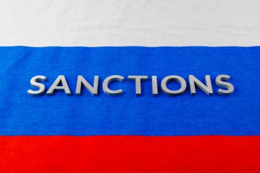 the word sanctions laid with silver metal letters on russian tricolor flag