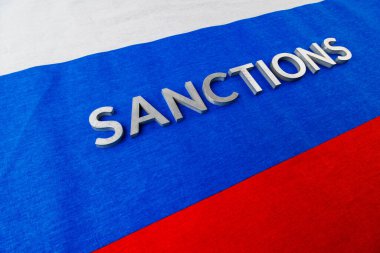 the word sanctions laid with silver metal letters on russian tricolor flag in diagonal perspective
