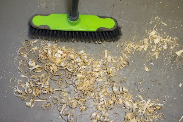 A small pile of wood shavings on a gray linoleum floor with a broom brush — Stockfoto