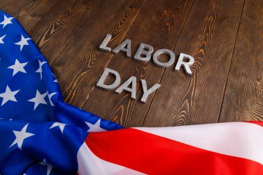 words labor day laid with silver metal letters on wooden surface with crumpled USA flag on bottom side