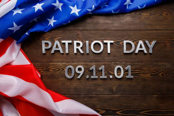De woorden patriot dag gelegd met zilveren metalen letters op houten plank oppervlak met verkreukelde usa vlag — Stockfoto