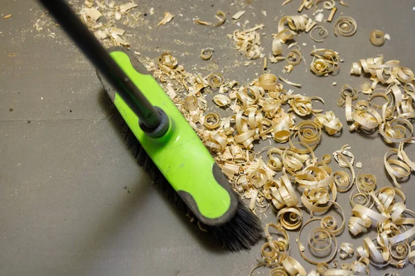 A small pile of wood shavings on a gray linoleum floor with a broom brush — Fotografia de Stock