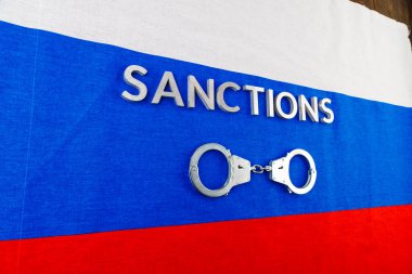 the word sanctions laid with silver metal letters on russian tricolor flag near handcuffs in directly above view