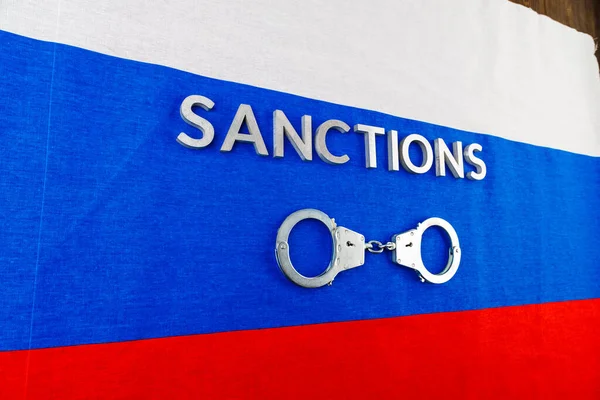 the word sanctions laid with silver metal letters on russian tricolor flag near handcuffs in directly above view