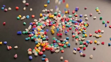 crushed colored stones sprinklig on black surface, forming a small pile, slo-mo