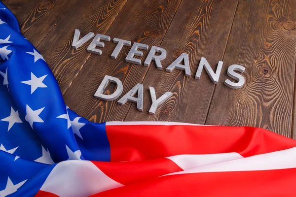 De woorden veteranen dag gelegd met zilveren metalen letters op houten plank oppervlak met verkreukelde usa vlag — Stockfoto