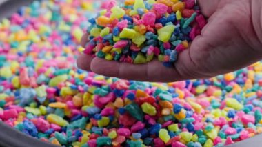 hand pouring crushed colored stones on flat surface with slo-mo