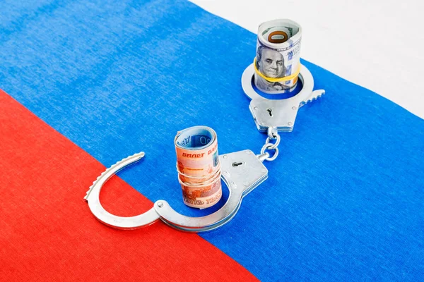 Roll of us dollar banknotes in a handcuffs with a roll of russian ruble banknotes on flat full-frame russian flag background — Foto de Stock