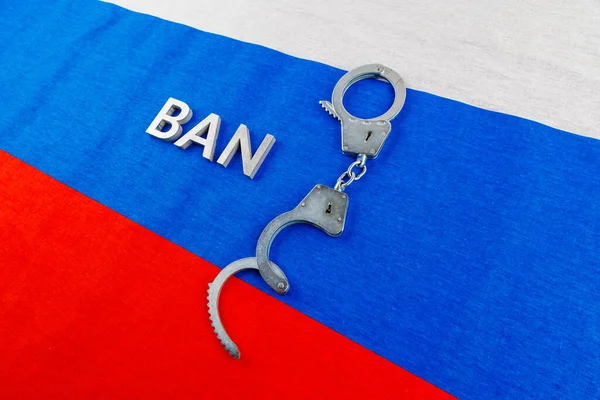 The word ban laid with silver metal letters and handcuffs over fabric Russian Federation flag — 스톡 사진