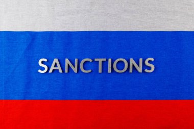 the word sanctions laid with silver metal letters on russian tricolor flag