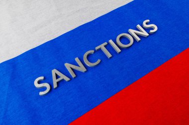 the word sanctions laid with silver metal letters on russian tricolor flag in diagonal perspective