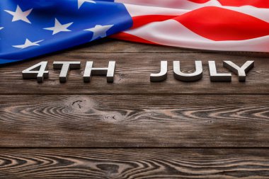 words 4th july and crumpled usa flag on flat textured wooden surface background