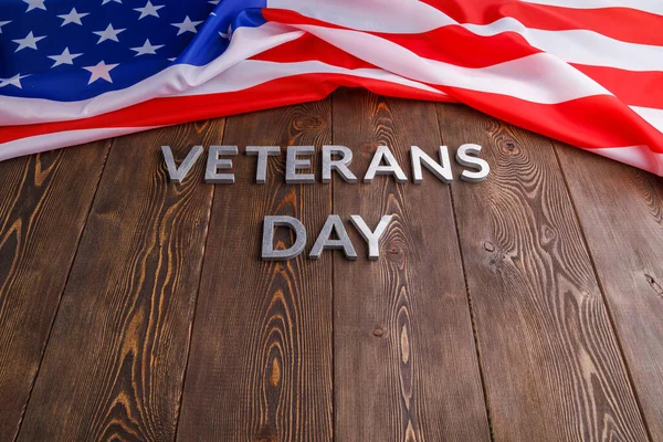 Slova veteráni den položený stříbrnými kovovými písmeny na dřevěném povrchu desky se zmačkanou americkou vlajkou — Stock fotografie