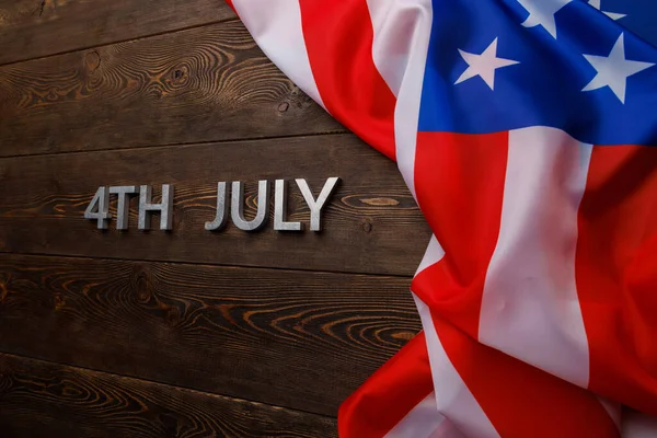 The words 4th july and crumpled usa flag on flat textured wooden surface background — Stock Photo, Image