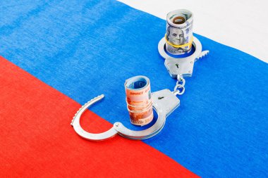 roll of us dollar banknotes in a handcuffs with a roll of russian ruble banknotes on flat full-frame russian flag background
