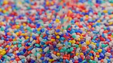colored stones puring on flat surface, forming a small pile rotating in slo-mo