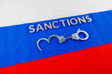 the word sanctions laid with silver metal letters on russian tricolor flag near handcuffs in directly above view