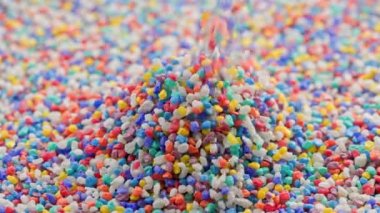 crushed colored stones puring on flat surface, forming a small pile in slo-mo