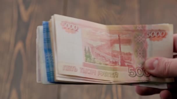 Hand shaking small stack of russian ruble banknotes over wooden background — Stok video