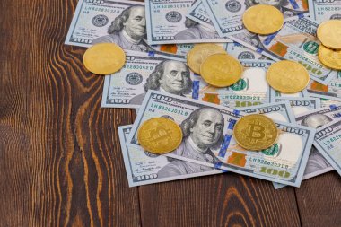 bitcoin coins scattered over US dollar paper banknotes on wooden background
