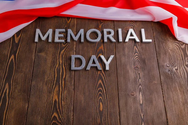 The words memorial day laid with silver metal letters on wooden board surface with crumpled usa flag below — Zdjęcie stockowe