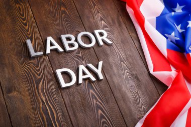 Tahta yüzeyde gümüş metal harflerle, sol tarafında buruşuk Amerikan bayrağıyla...