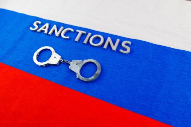 the word sanctions laid with silver metal letters on russian tricolor flag near handcuffs in directly above view