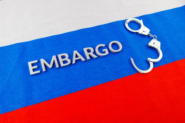 The word embargo laid with silver metal letters on russian tricolor flag with silver handcuffs — Foto Stock