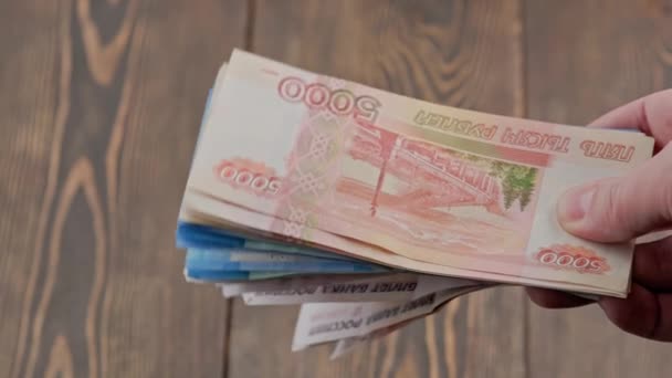 Hand shaking small stack of russian ruble banknotes over wooden background — Stockvideo