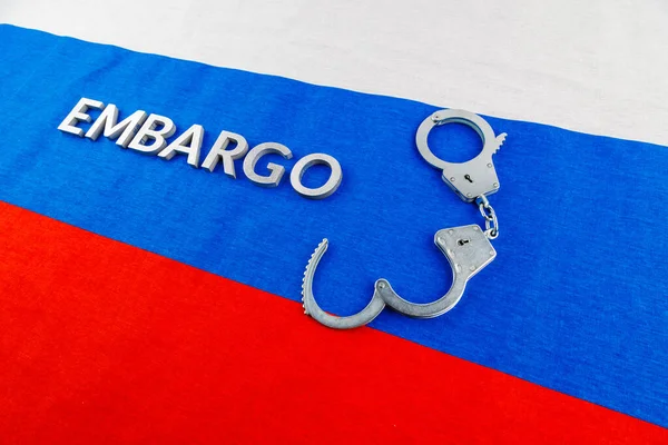The word embargo laid with silver metal letters on russian tricolor flag with silver handcuffs — Foto Stock