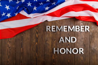 words remember and honor laid with silver metal letters on wooden background with USA flag above
