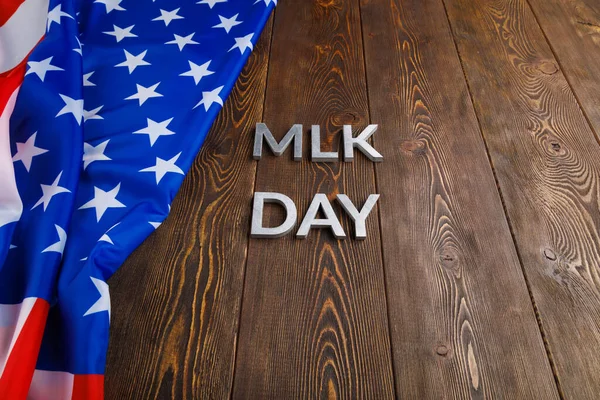 the word MLK day laid with silver metal letters on wooden surface with crumpled USA flag at left side