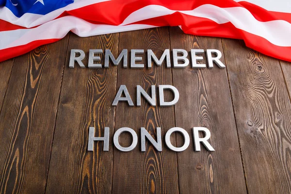 Words remember and honor laid with silver metal letters on wooden background with USA flag on the far side — Stockfoto