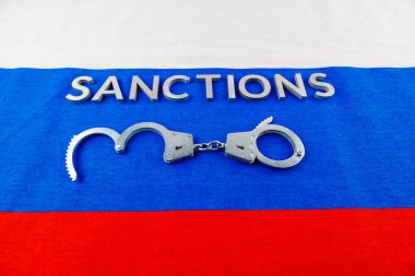 the word sanctions laid with silver metal letters on russian tricolor flag near handcuffs in directly above view