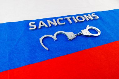 the word sanctions laid with silver metal letters on russian tricolor flag near handcuffs in directly above view