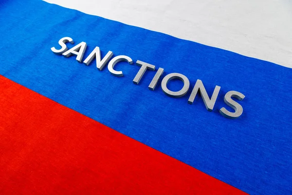 the word sanctions laid with silver metal letters on russian tricolor flag in diagonal perspective