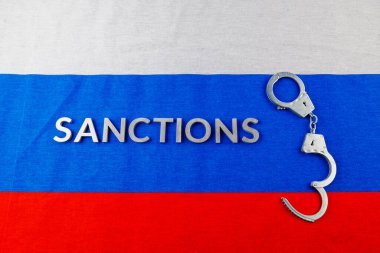 the word sanctions laid with silver metal letters on russian tricolor flag near handcuffs in directly above view