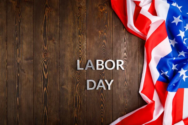 Words labor day laid with silver metal letters on wooden surface with crumpled USA flag on right side — Stock Photo, Image