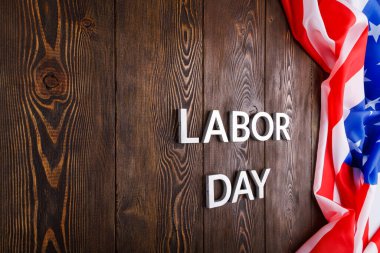 Tahta yüzeyde gümüş metal harflerle, sol tarafında buruşuk Amerikan bayrağıyla...