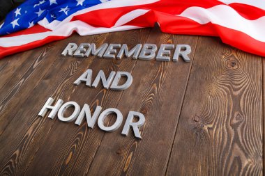 words remember and honor laid with silver metal letters on wooden background with USA flag above