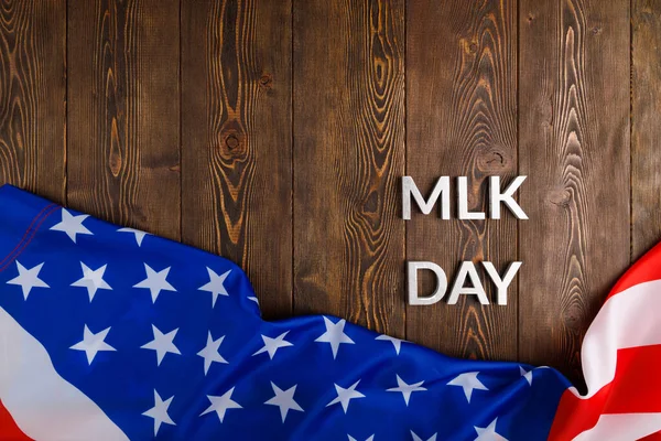 the word MLK day laid with silver metal letters on wooden surface with crumpled USA flag at lower side