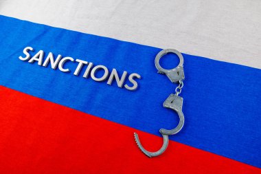 the word sanctions laid with silver metal letters on russian tricolor flag near handcuffs in directly above view