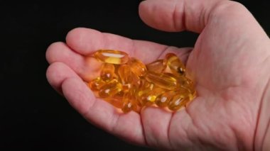 caucasian hand holding handful of yellow tramsparent pills of fish oil on black